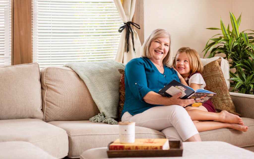 Senior Care Plus Insured Grandmother with grandchild on a sofa reading book